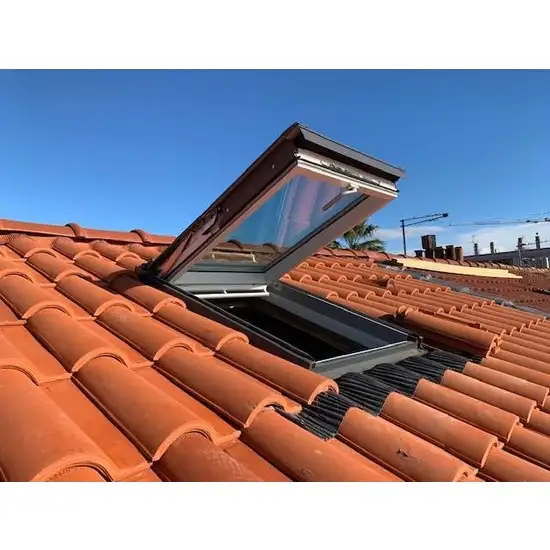 Fenêtre de toit velux ouverte sur une toiture en tuiles